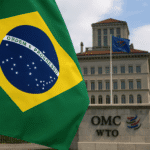 Bandeira do Brasil em frente ao prédio da OMC em Genebra, representando ação comercial formal. Brasil aciona a OMC.